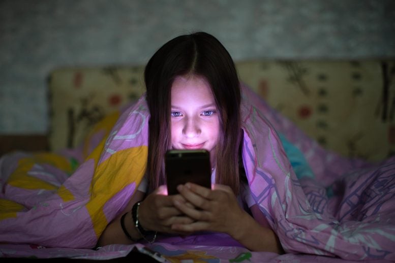 Gadis remaja di bawah selimut menjelajahi telepon