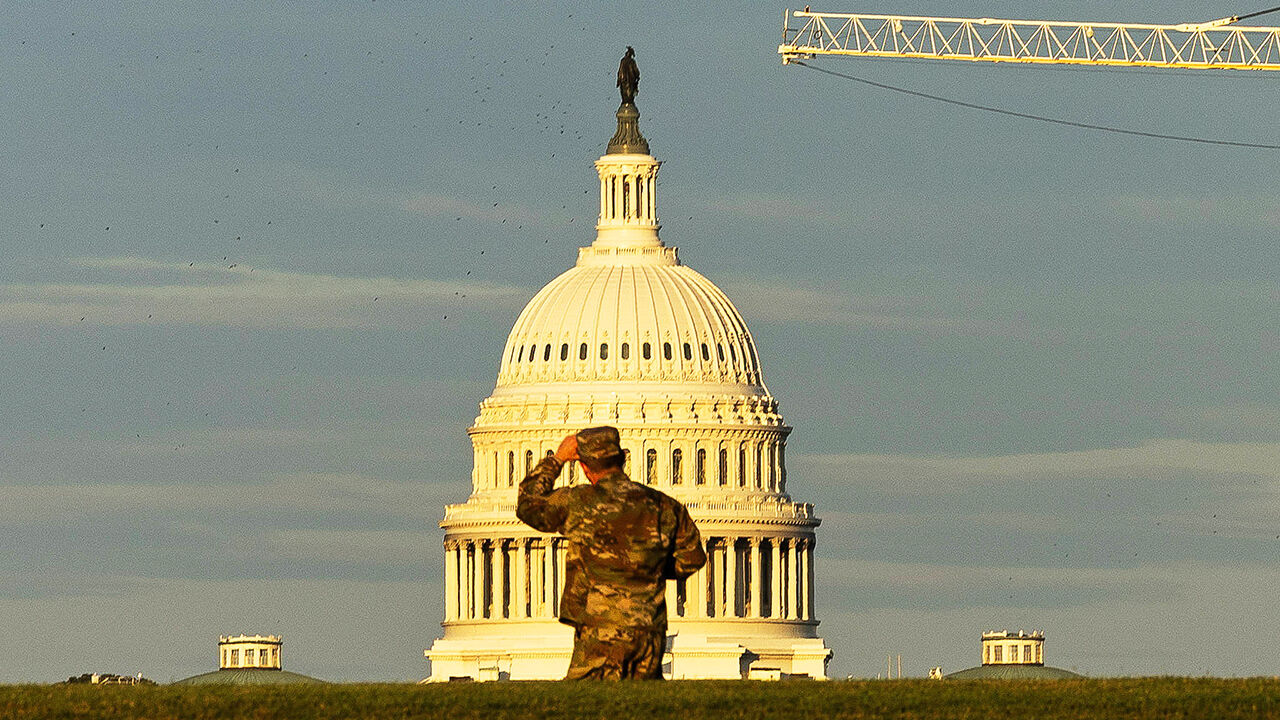 A member of the National Guard adjusts their cap while looking at the US Capitol