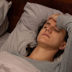 Wanita muda yang lelah melelahkan berbaring di tempat tidur memegangi kepalanya